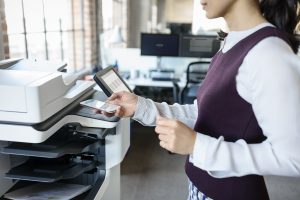 woman standing near printer sending something to print from her mobile phone